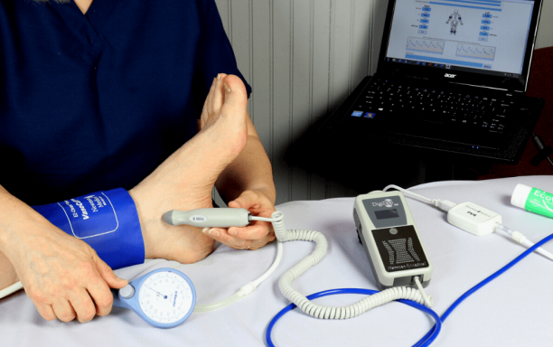 A person measuring blood pressure on an ankle with a digital monitor nearby.