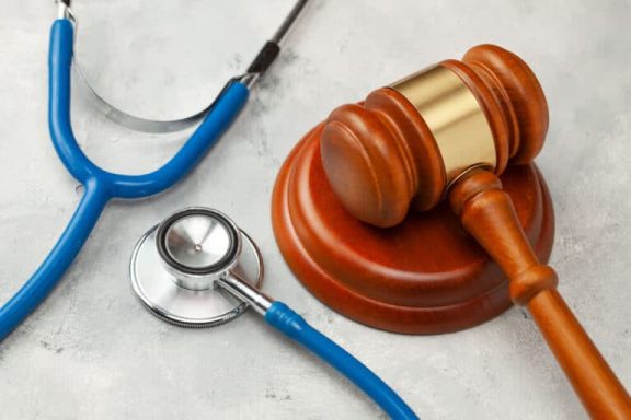 A wooden gavel beside a stethoscope on a textured surface.